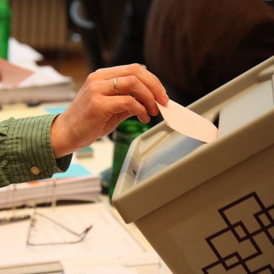 Hand legt Stimmzettel in Wahlurne