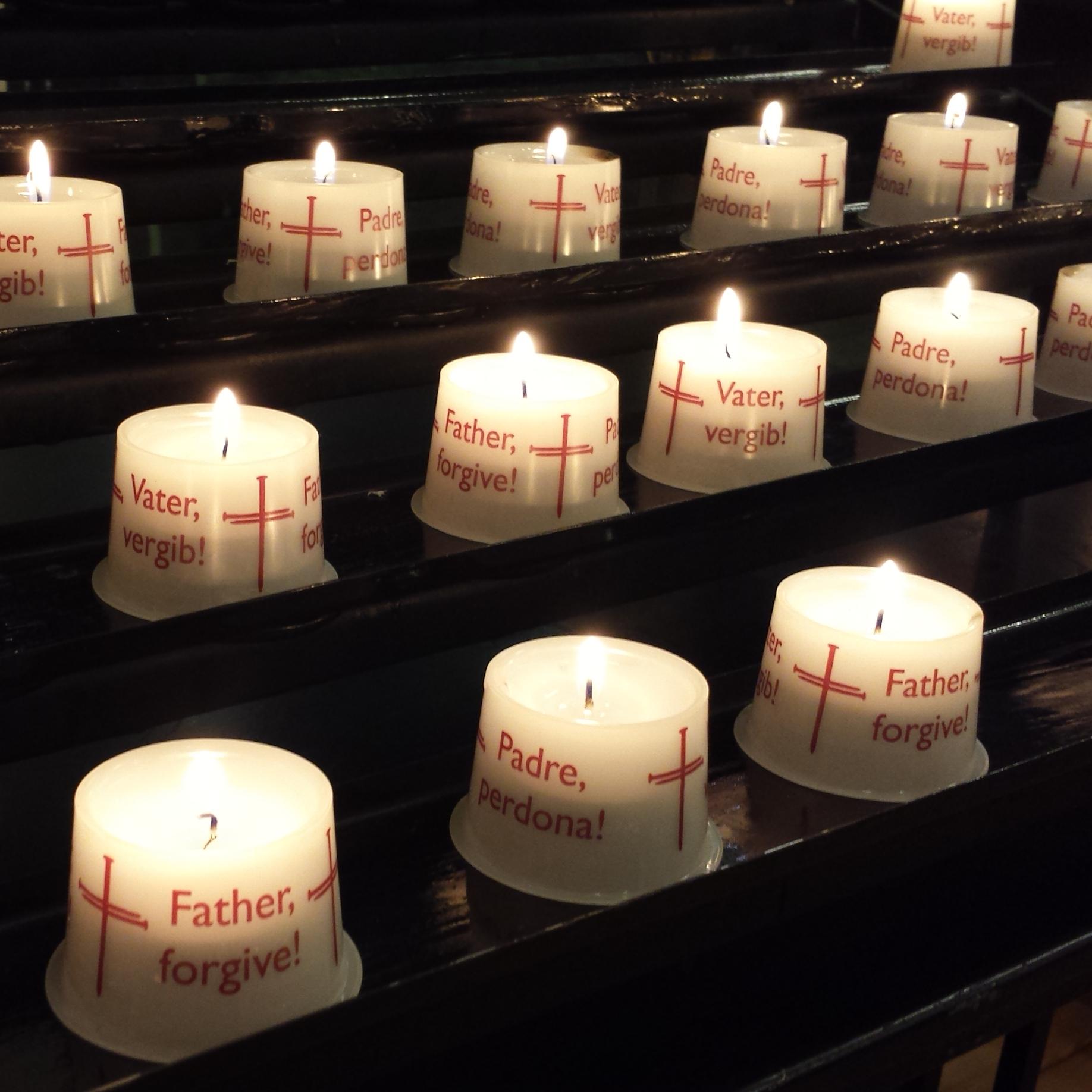 Kerzen in der Nagelkreuzkapelle mit der Aufschrift "Vater, vergib" in mehreren Sprachen
